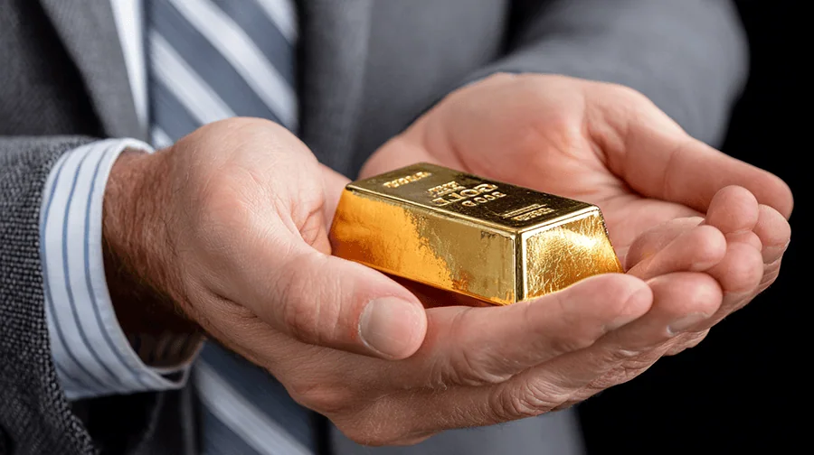 Eine Person hält einen goldenen Barren in beiden Händen, der glänzend und in einer eleganten Präsentation ist.
